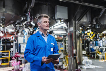 Mature technician day dreaming while holding digital tablet in factory - DIGF14078