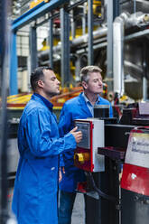 Male engineers examining machinery equipment in industry - DIGF14080