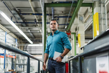 Confident male professional with digital tablet looking away in factory - DIGF14103