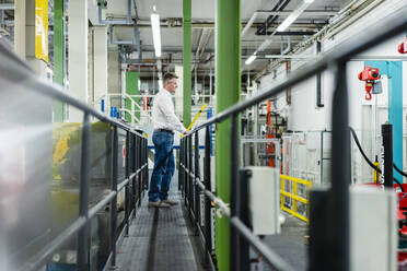 Male supervisor standing on footpath while looking at machinery in industry - DIGF14107