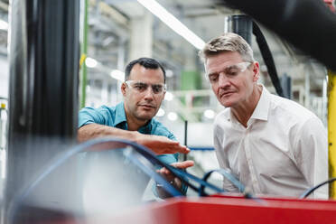 Male professional discussing with colleague while examining machinery equipment in factory - DIGF14112