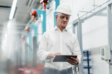 Mature male technician wearing hardhat working in digital tablet in industry - DIGF14118