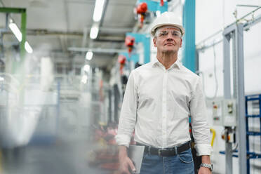 Selbstbewusster reifer Manager mit Brille und Schutzhelm, der in einer Fabrik nachdenkt - DIGF14119