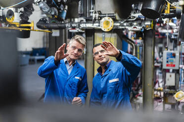 Male professionals gesturing while examining manufacturing equipment in industry - DIGF14139