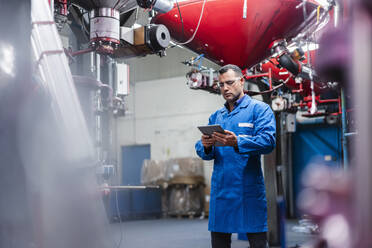 Reifer männlicher Techniker bei der Arbeit an einem digitalen Tablet an einer Maschine in einer Fabrik - DIGF14144