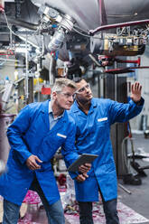 Männliche Mitarbeiter mit digitalem Tablet diskutieren bei der Überprüfung von Maschinen in einer Fabrik - DIGF14149