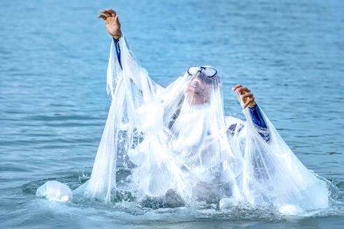 Mature man covered with plastic screaming while swimming in sea - GGGF00734