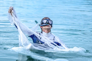 Älterer Mann mit Tauchermaske reißt Plastik im Meer - GGGF00736