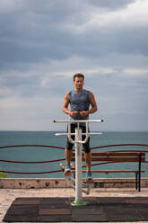 Erwachsener Mann trainiert am Morgen auf Sportgeräten am Meer - CAVF91436