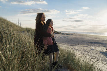 Mutter und Tochter am Strand stehend mit Blick aufs Meer - CAVF91438