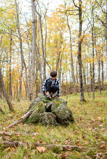 Kleiner Junge klettert an einem Herbsttag auf einen großen Felsen im Wald. - CAVF91457