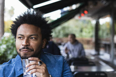 Nahaufnahme eines Hippie-Mannes mit Afro-Haar, der in einem Straßencafé Wasser trinkt - PNAF00460