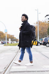 Hipster Mann mit Rucksack zu Fuß auf der Straße gegen klaren Himmel - PNAF00473