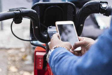 Hände eines Mannes, der sein Smartphone benutzt, um an einer Parkstation ein Fahrrad zu mieten - PNAF00475