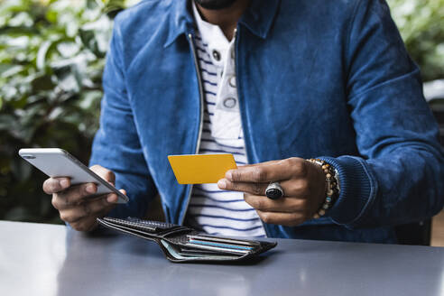 Nahaufnahme eines Mannes mit Kreditkarte, der in einem Straßencafé mobil bezahlt - PNAF00493
