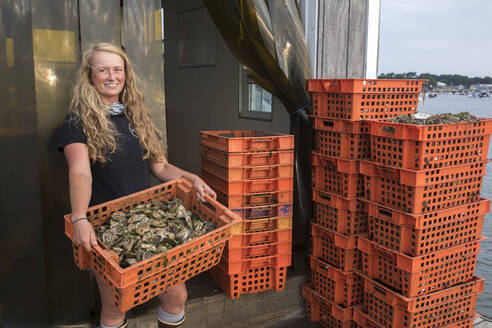 Female shellfish farmer holding crate of oysters - CAVF91485