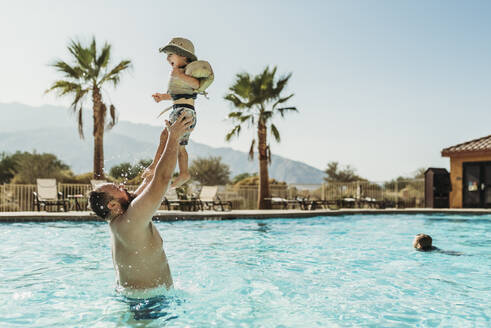 Vater wirft kleinen Jungen in die Luft, während er im Urlaub im Pool spielt - CAVF91499