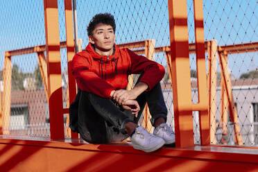Nachdenklicher junger Mann sitzt auf dem Geländer einer Brücke - OGF00749