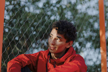 Close-up of thoughtful young man sitting against fence - OGF00759