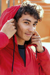 Porträt eines lächelnden jungen Mannes mit roter Kapuze in Großaufnahme - OGF00769