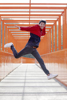 Carefree young man jumping on footbridge - OGF00770