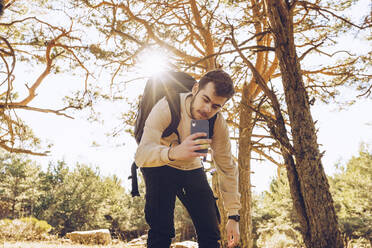 Männlicher Wanderer, der im Wald stehend mit seinem Smartphone fotografiert - RSGF00471