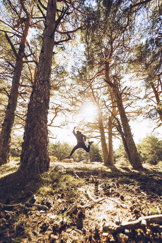 Fröhlicher junger Mann, der im Wald auf das Land springt, lizenzfreies Stockfoto