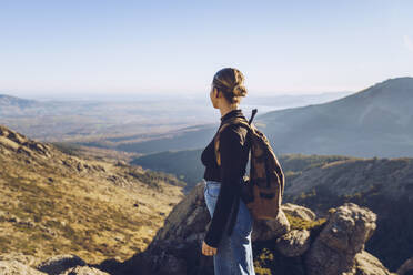Weiblicher Wanderer mit Rucksack, der auf dem Gipfel eines Berges steht und die Aussicht betrachtet - RSGF00479