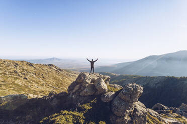 Young man with arms outstretched standing on mountain against clear sky - RSGF00482