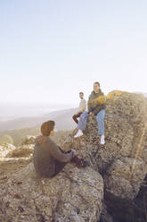 Freunde unterhalten sich auf dem Gipfel eines Berges bei klarem Himmel an einem sonnigen Tag - RSGF00486