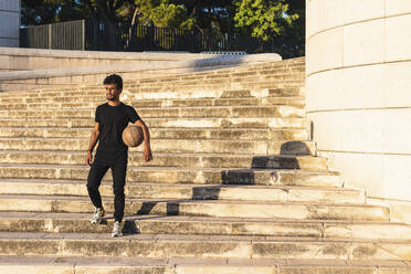 Junger Mann mit Basketball, der sich bei Sonnenuntergang auf einer Treppe nach unten bewegt - PNAF00517