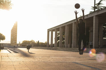 Junger Mann spielt Basketball auf dem Fußweg gegen den klaren Himmel bei Sonnenuntergang - PNAF00519