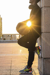 Sun shining through young man holding basketball while standing by wall at sunset - PNAF00525