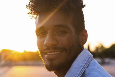 Nahaufnahme eines lächelnden jungen Mannes gegen den klaren Himmel bei Sonnenuntergang - PNAF00531