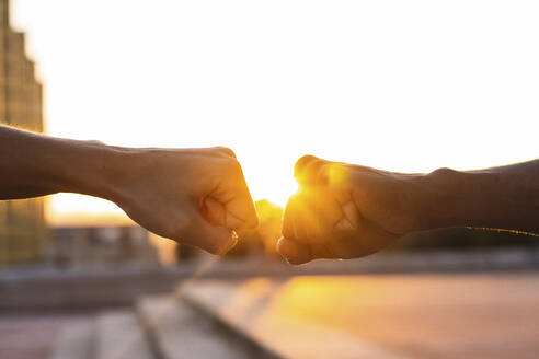 Hands of friends giving fist bump to each other against clear sky during sunset - PNAF00532