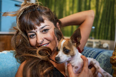 Nahaufnahme einer Hippie-Frau mit Chihuahua auf dem Sofa zu Hause - GGGF00741