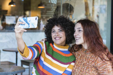 Lächelnde Freunde, die ein Selfie mit ihrem Mobiltelefon machen, während sie im Restaurant sitzen - PNAF00550