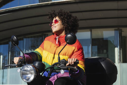 Lächelnde Frau mit Sonnenbrille, die wegschaut, während sie auf einem Motorrad sitzt - PNAF00553