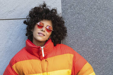 Young woman wearing sunglasses smiling while leaning on wall - PNAF00571