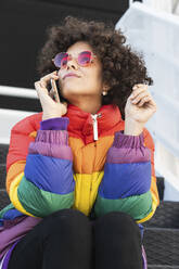 Frau mit mehrfarbiger Jacke, die auf einer Treppe sitzend mit einem Mobiltelefon spricht - PNAF00572
