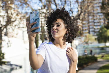 Smiling woman taking selfie through mobile phone while standing outdoors - PNAF00575