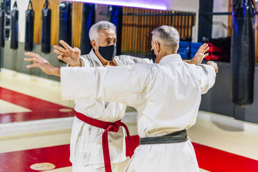 Männer mit ausgestreckten Armen, die Gesichtsmasken tragen, während sie im Fitnessstudio Karate üben - OCMF01973