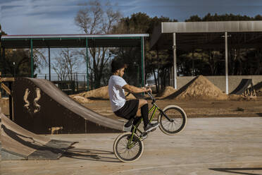 Young man doing wheelie at bike park on sunny day - ACPF01013