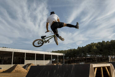 Man doing stunt over ramp at bike park against sky - ACPF01020