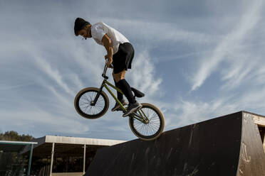 Junger Mann springt auf Rampe in Fahrradpark gegen Himmel - ACPF01022