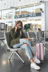 Junge Frau mit Gesichtsmaske, die am Bahnhof sitzt und über ein Smartphone spricht - JAQF00132