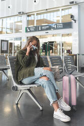 Young woman wearing face mask talking over smart phone while sitting at railroad station - JAQF00132