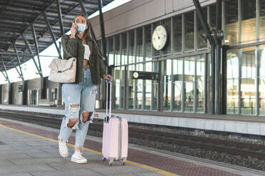 Frau mit Gesichtsmaske, die am Bahnsteig über ihr Smartphone spricht - JAQF00134