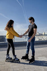 Young couple with roller skate standing on pier against sky - VEGF03521