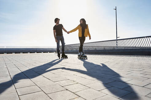 Junges Paar, das sich beim Rollschuhlaufen auf dem Pier an einem sonnigen Tag ansieht - VEGF03525